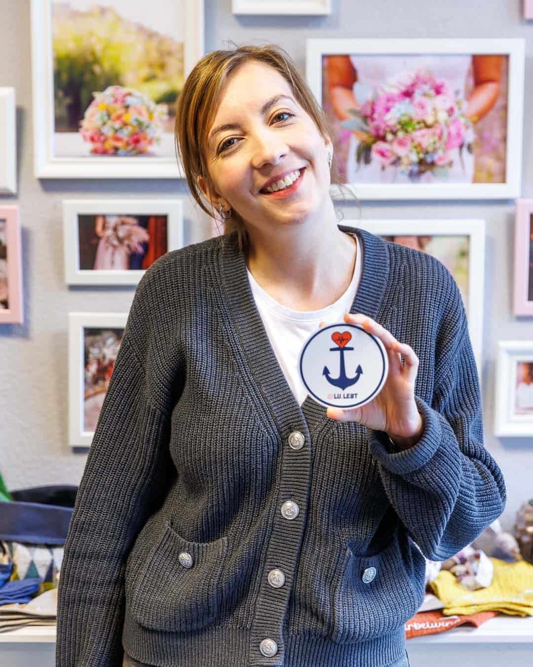 Vanessa von Blütenzauber in Ludwigshafen Süd hält einen Lu.lebt! Sticker in die Kamera
