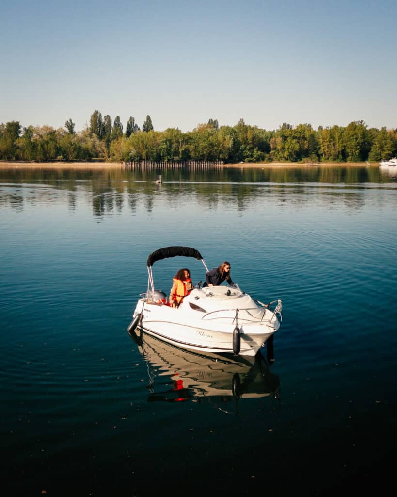 Dominique ist mit Schülerin auf dem Boot und übt Manöver, im Hintergrund Wasser und eine Insel