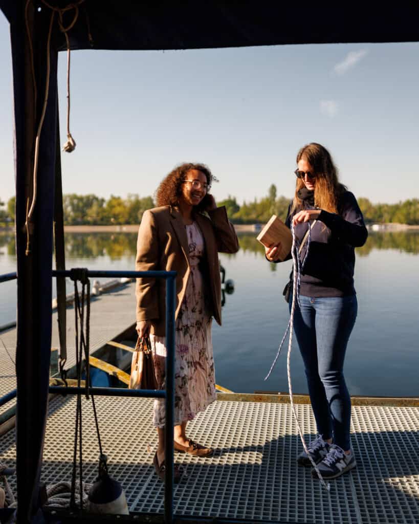 Dominique steht mit einer Schülerin am Wasser und bindet Knoten, beide Lachen und haben Spaß
