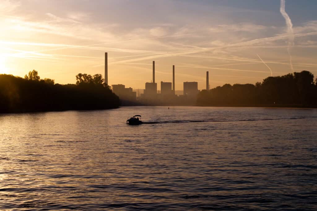 Das Schulungsboot "Kleene" morgens bei Sonnenaufgang auf dem Rhein, im Hintergrund das Großkraftwerk Mannheim