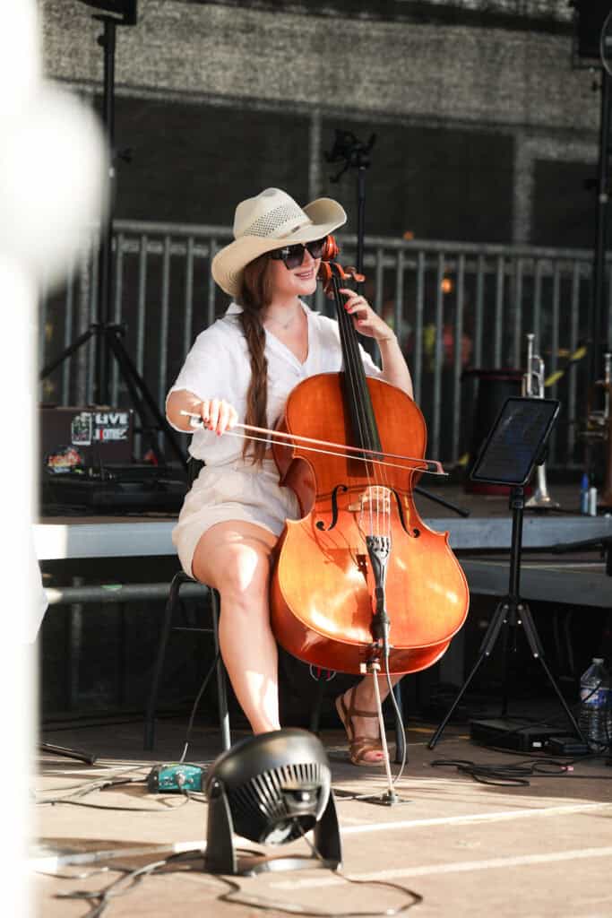 Frau spielt Cello und hat einen Hut auf